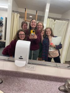 5 girls taking a picture in a bathroom mirror while holding a ladder