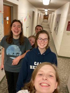 5 girls laughing in a hallway while taking a selfie